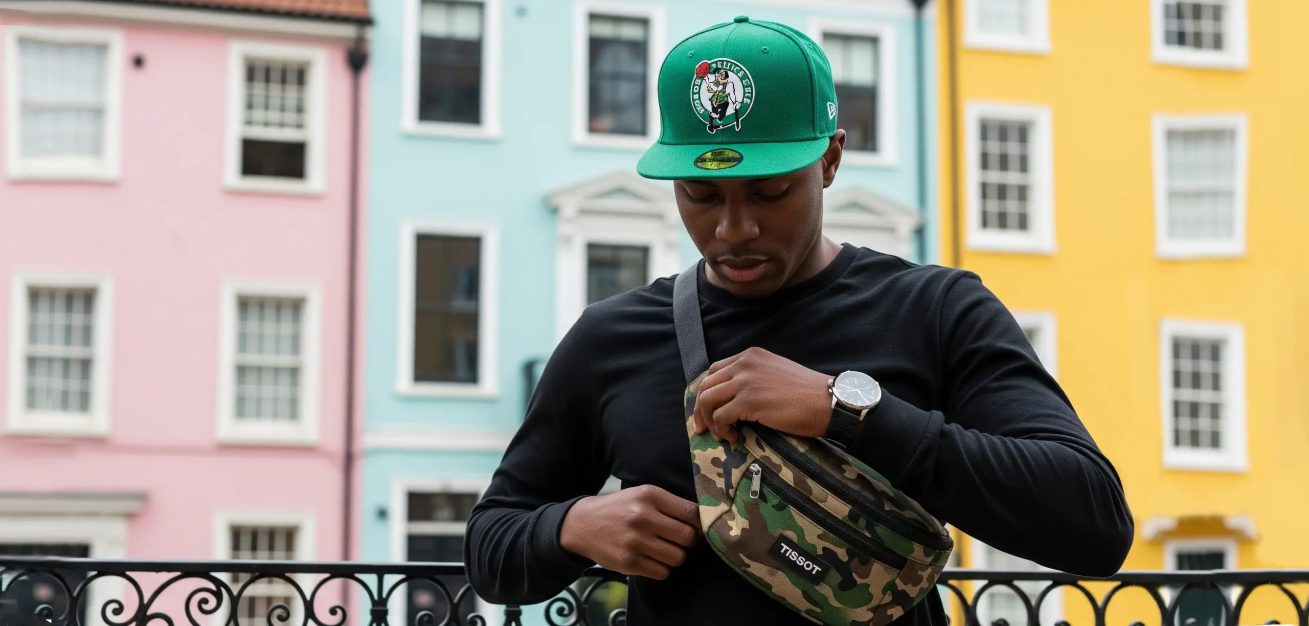 a young boy wearing a green boston celtic baseball cap with a camo bag around his chest
